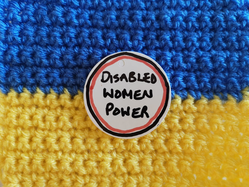 Crocheted Ukrainian flag with a label reading 'disabled women power'. Vici Wreford-Sinnott