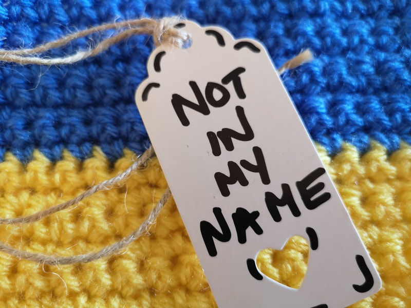 A crocheted Ukrainian flag with a label reading, 'not in my name'. Vici Wreford-Sinnott.