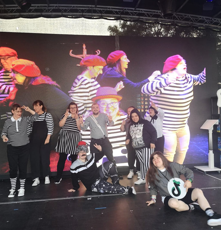 All company members in black and white stripy outfits posing in front of a large projection promoting their show 