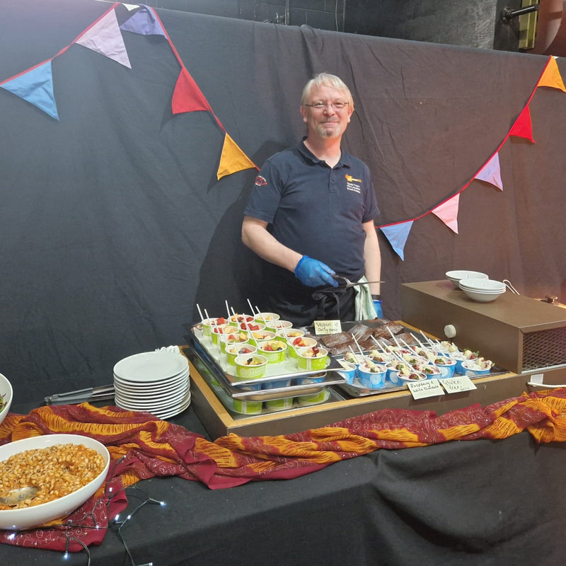 A smiling older man serving at the dessert section of the buffet. Bunting in the background. 