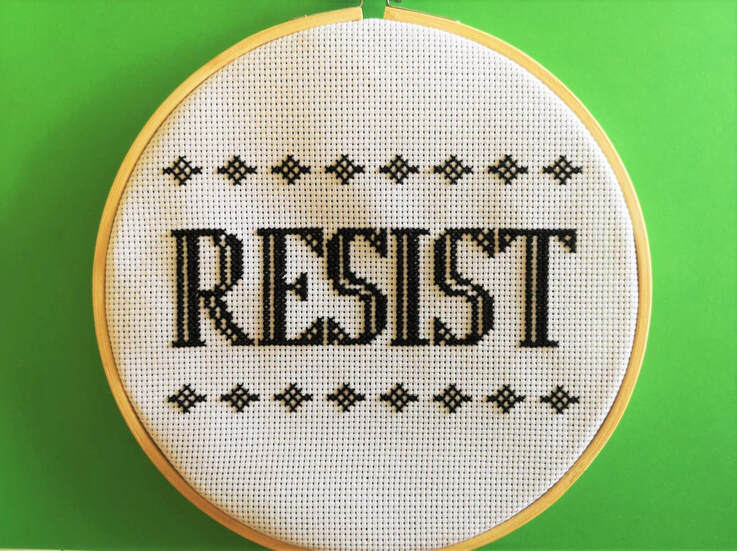 Circular bamboo hoop with white fabric and the cross stitched word RESIST in bold capital letters. A line of diagonal shapes above and below the word. All on a bright green background. 