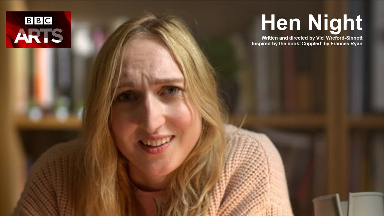 Actor Nicola Chegwin is pictured in a film still from Hen Night, playing the solo lead part of Jessica. Nicola is a young white woman with long blond hair. She is wearing a large ovesized pale pink cardigan and pyjamas. She is seated at a desk which is out of shot, but we can see her crutch is leaning against it next to her. She is talking, and looking into the camera quizzically. Text reads BBC Arts, Hen Night written and directed by Vici Wreford-Sinnott, inspired by the book 'Crippled' by Frances Ryan. Film Still Credit: Rhys Fagan.Picture