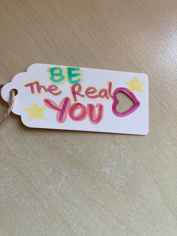 Colourful lettering on a white parcel label - 'Be the real you'