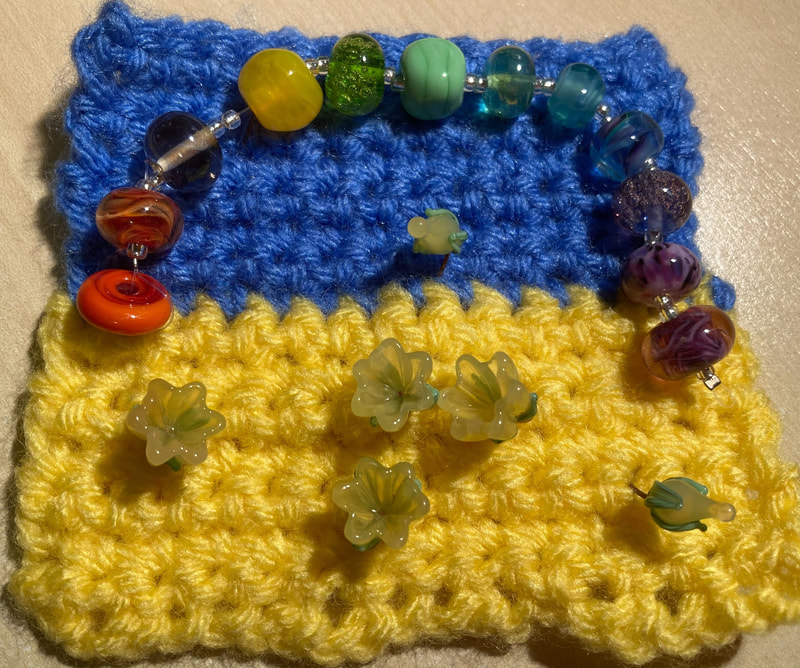 A crocheted Ukranian flag with a rainbow of handmade glass beads and glass bead flowers. Caroline Miles. 