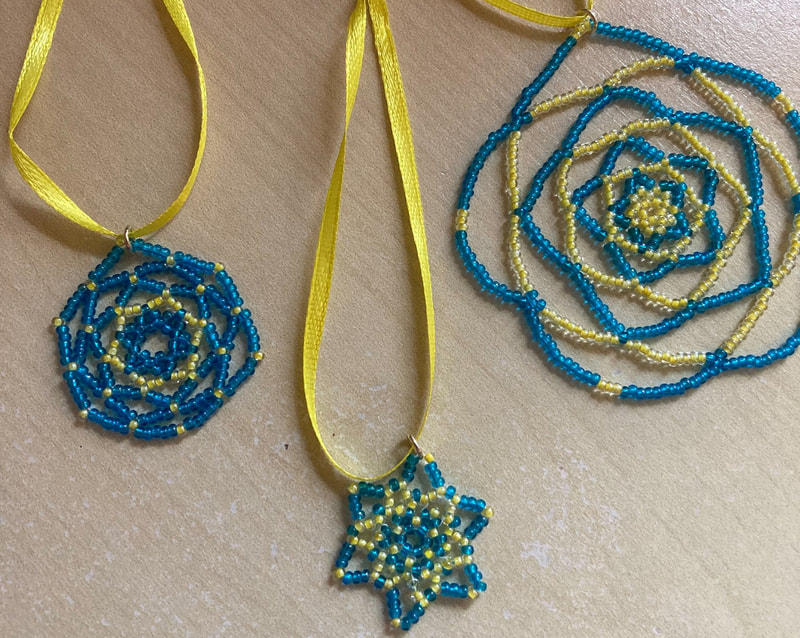 3 pendants on yellow ribbons. Blue and yellow glass beads, each in a different mandala style. Caroline Miles. 