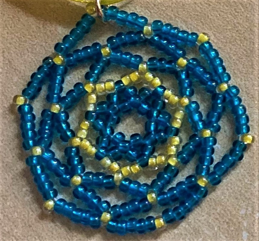 A blue and yellow pendant, handmade with small glass beads with stars at its centre.  Caroline Miles.