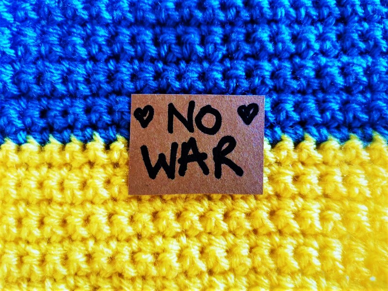 A blue and yellow crochet flag with No War and a love heart written on it. Vici Wreford-Sinnott