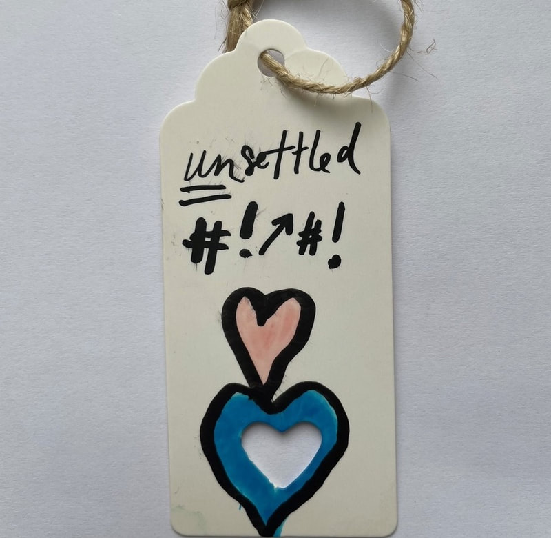 White parcel label saying 'UNsettled' with 'un' underlined. #!upward arrow#! A pink love heart on top of a blue loveheart. Samantha Blackburn