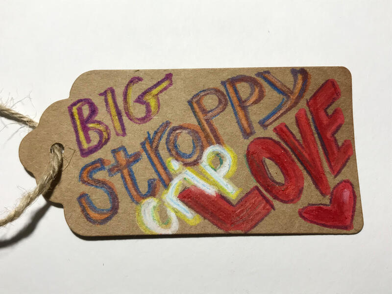 A brown parcel label with bold colourful lettering says 'Big stroppy crip love' with a hand drawn loveheart. Caroline Cardus