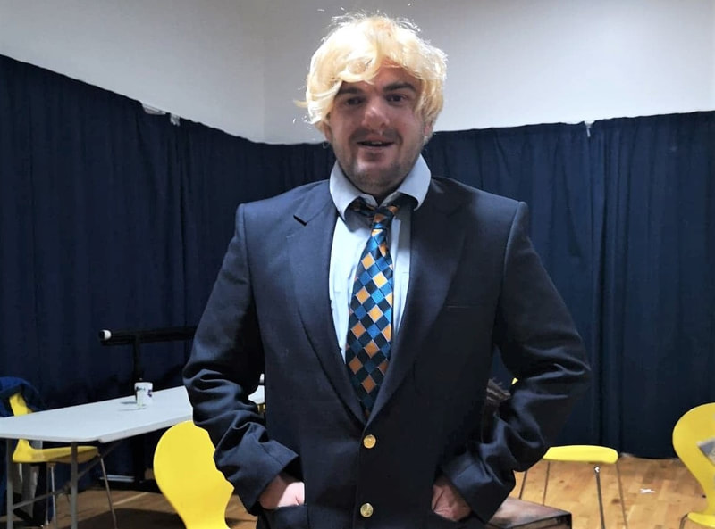 A young male actor in a Boris Johnson blonde wig, suit jacket, short and tie
