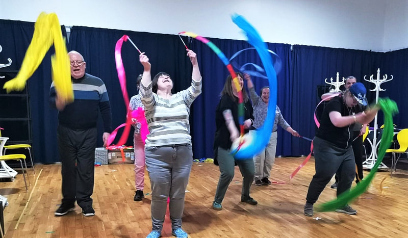 a group of six actors in a dance studio experimenting with colourful gym ribbons - all looking very happy