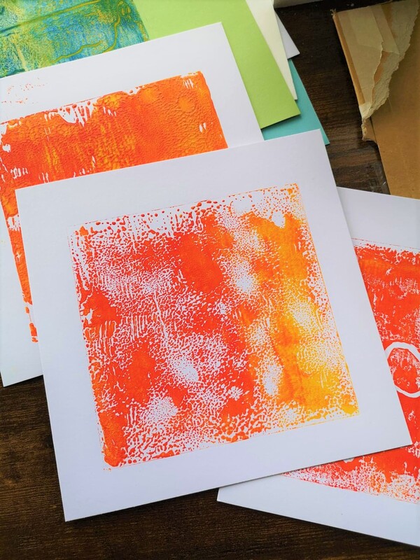 A pile of four cards loosely arranged - all white with either bold orange and yellow abstract prints and a blue and green one. 