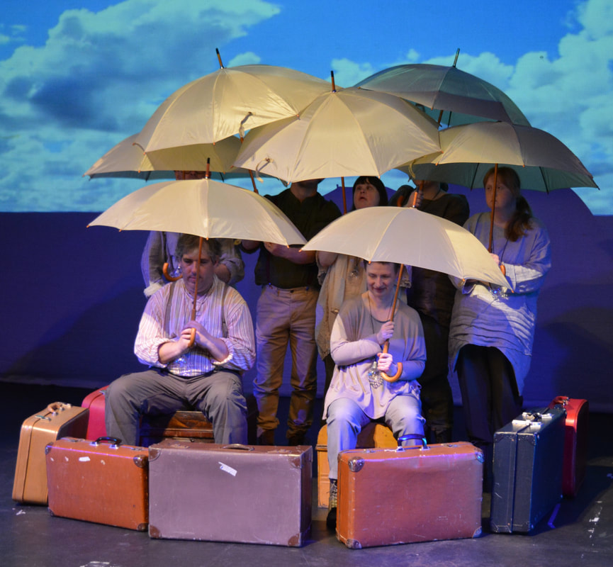 Another highly visual and imaginative show with lots of huge projections creating backgrounds. All props were multi-functional and helped to create a range of environments. The first image shows A group of actors in utilitarian costumes have created an airship using umbrellas and old suitcases. A bright blue sky with white clouds is projected behind them. 