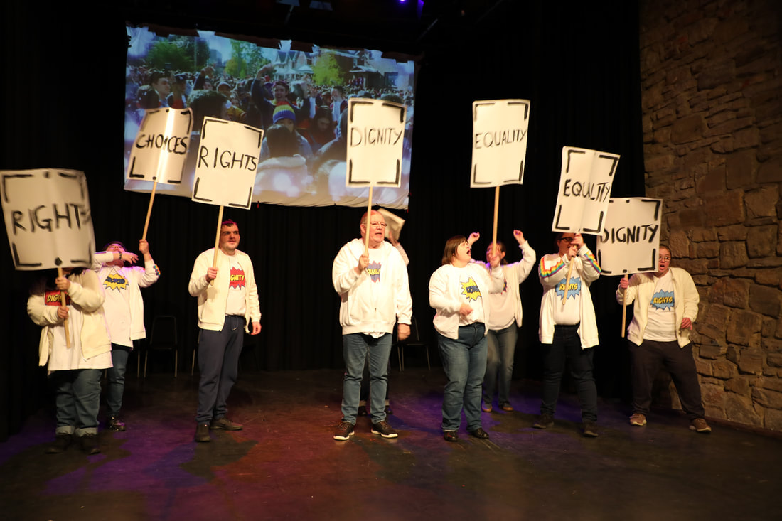 The first image shows 8 actors on stage in blue jeans, white bomber jackets and tee shirts which say words including equality, dignity, choices and rights. They are holding placards with the same words on them. 