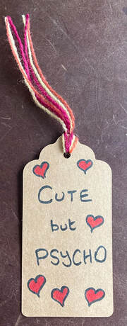 Brown Parcel label with handwriting - 'cute but psycho' and a handful of love hearts. Colourful thread.