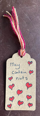 'May contain nuts' on a brown label surrounded by lots of red hearts. Colourful thread.