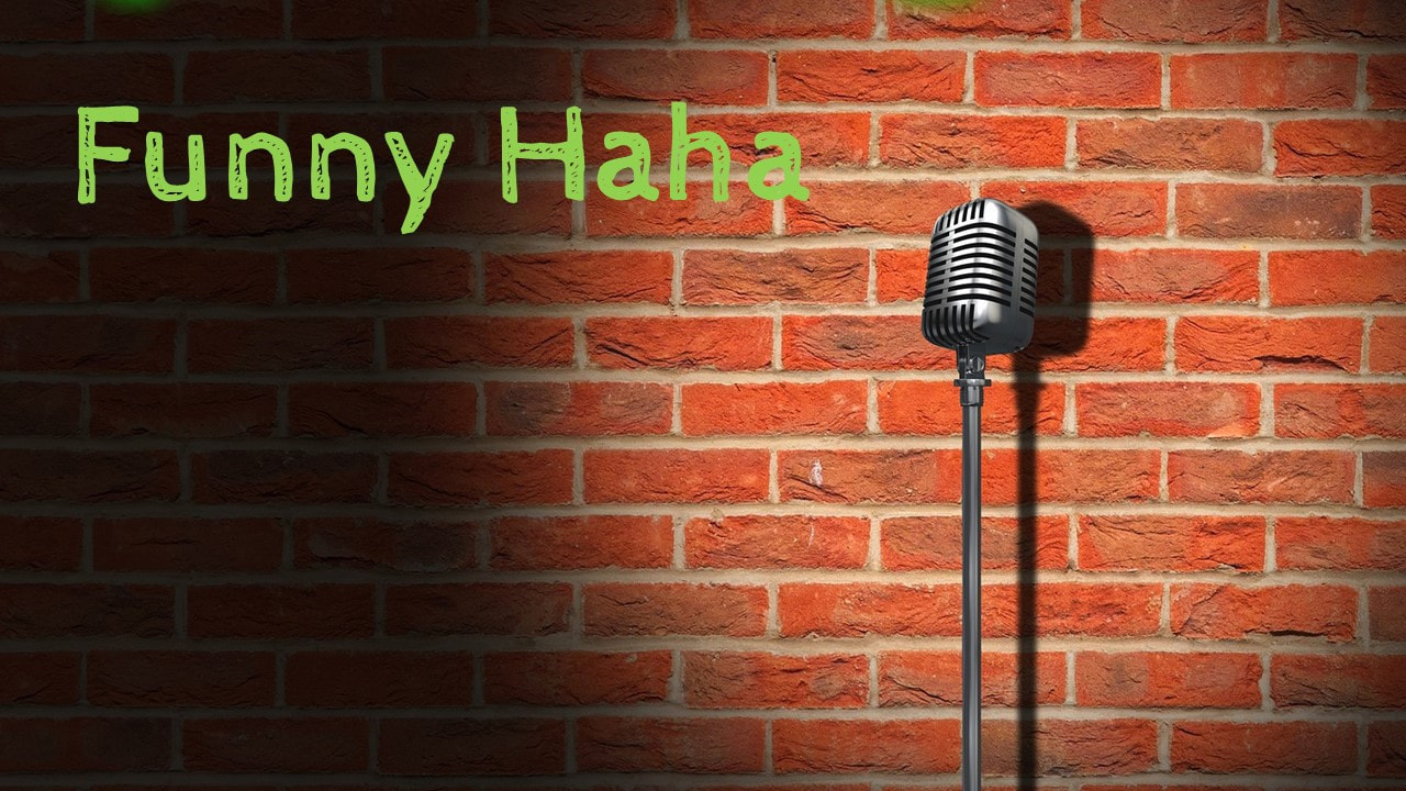 A red brick wall with the words Funny Ha Ha in green and an old fashioned microphone on a stand