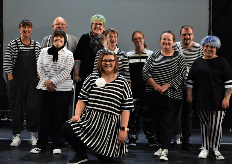 A company posed portrait - ten people wearing variations of black and white stripy tops, and a range of ages, all smiling together to the camera.