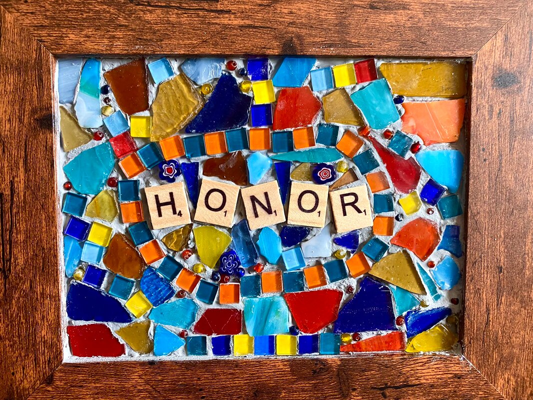 A beautiful multi coloured mosaic with a blue and orange border of small square glass tiles around the name Honor. Other irregular shaped glass mosaic pieces, blue, orange and hints of yellow with tiny round glass beads also placed in the grout. 