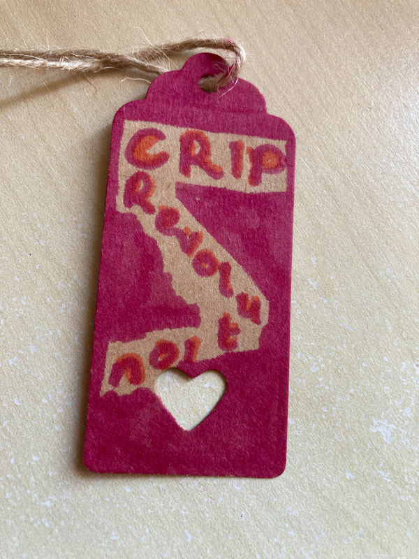 A label with a cut out heart and the words 'Crip Revolution' written in red, zig zagging down the label which is a dark marron colour. Caroline Miles