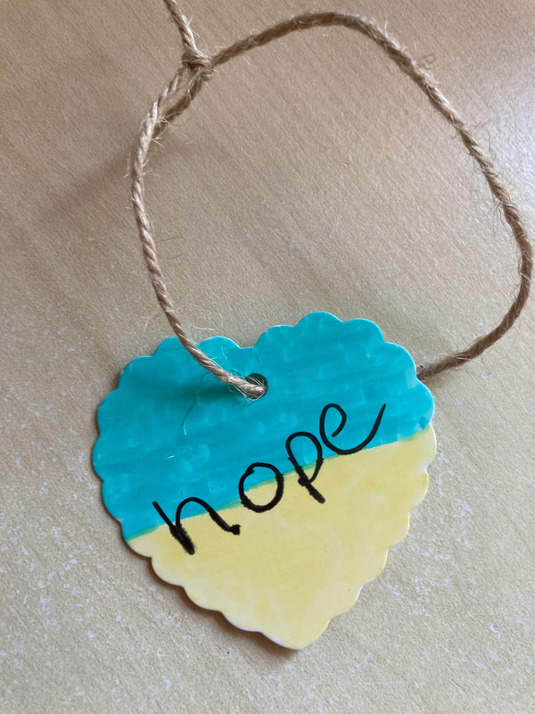 a heart parcel label coloured to reflect the Ukrainian flag with the word 'hope' written in black across it, hanging on a string. Caroline Miles.