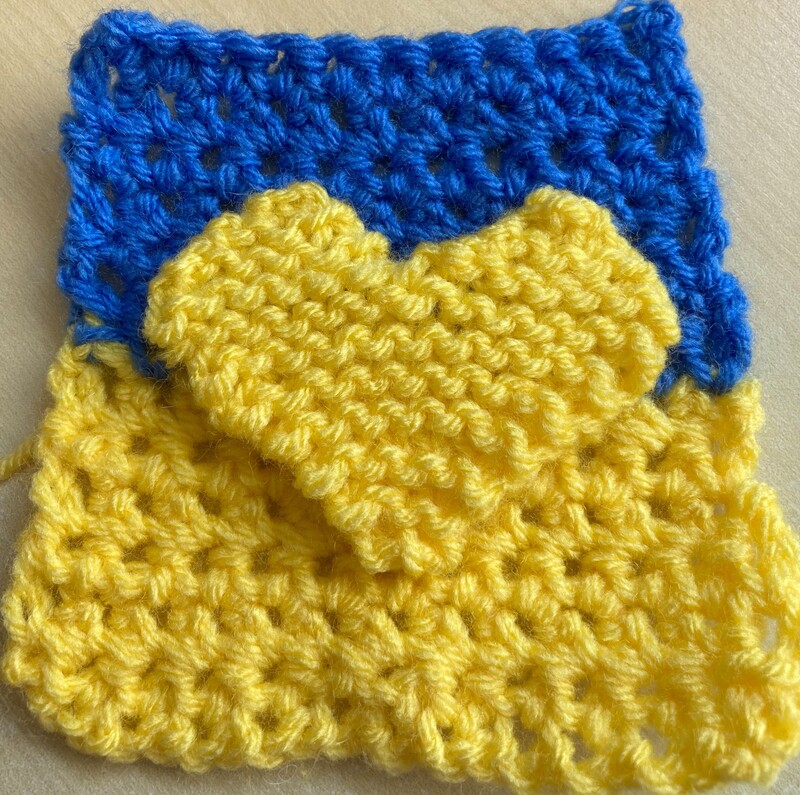 Crocheted Ukrainian flag with a knitted yellow heart on it. Caroline Miles