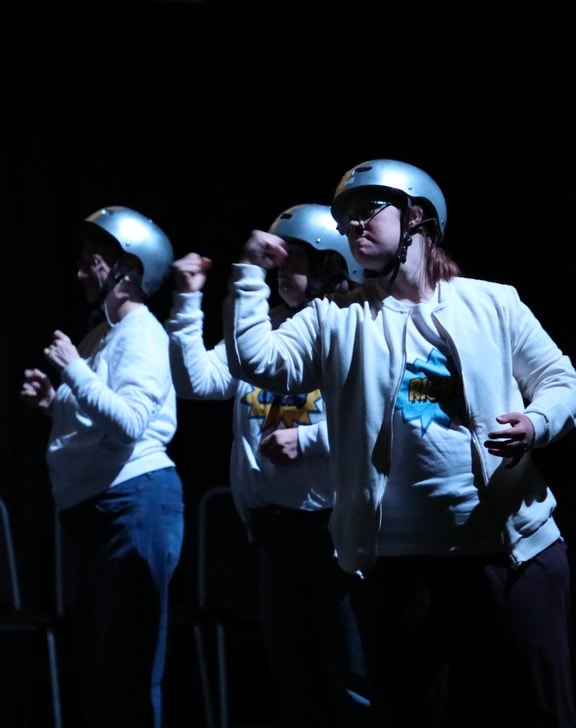 Three actors wearing silver skater helmets all with fists raised to an opposing bully offstage. They were doing Pinball Wizard reflecting being constantly being passed from pillar to post.