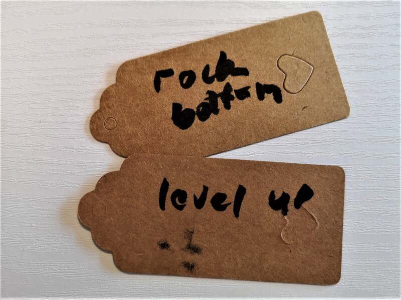 Image Description - 2 Brown parcel labels with handwritten text, 'rock bottom' and 'level up'. Pauline Heath