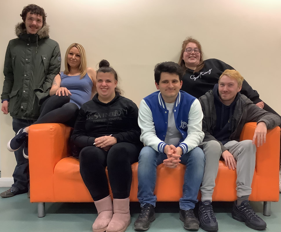 Six very happy smiley young actors from Jigsaw Theatre are all posing around a bright orange sofa, looking like they are ready to be creative. 